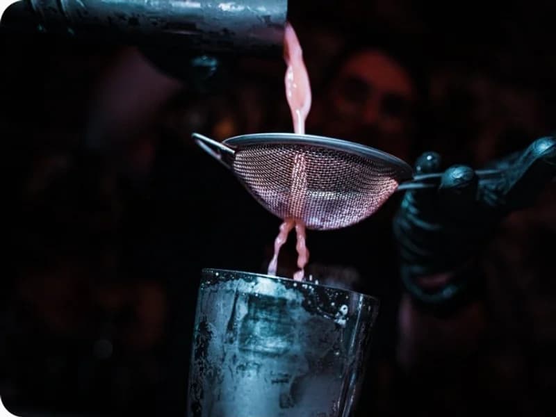 Un barman filtra un cocktail dentro al bicchiere